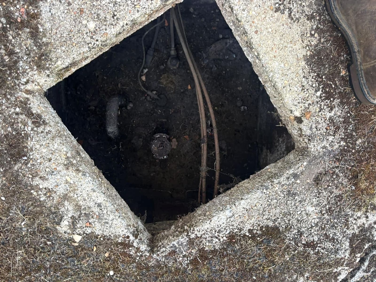 Regard en béton ouvert au-dessus d'une cuve à fioul enterrée, avec le trou d'homme et les conduites