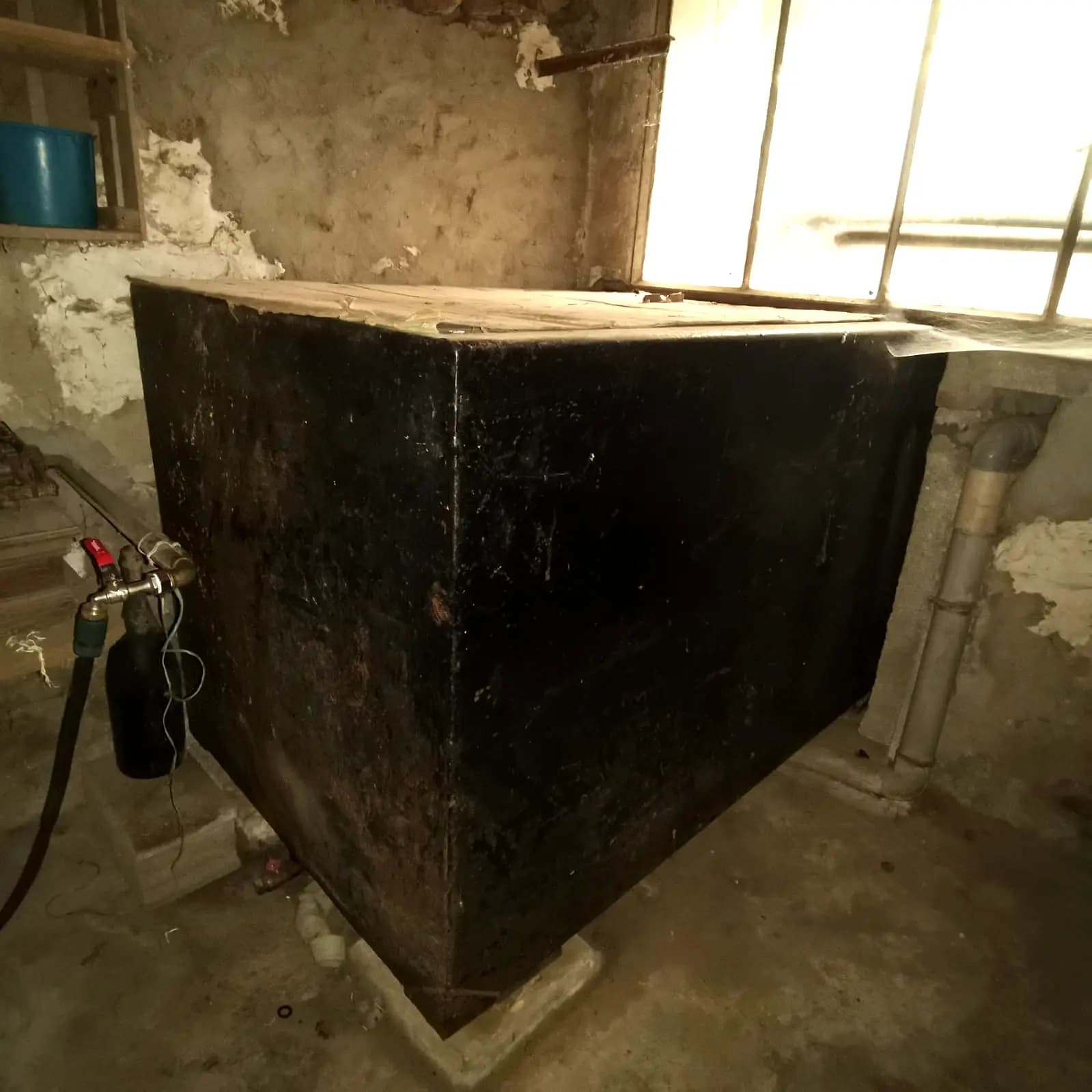 Cuve à fioul rectangulaire en acier noir dans une cave, sous un soupirail