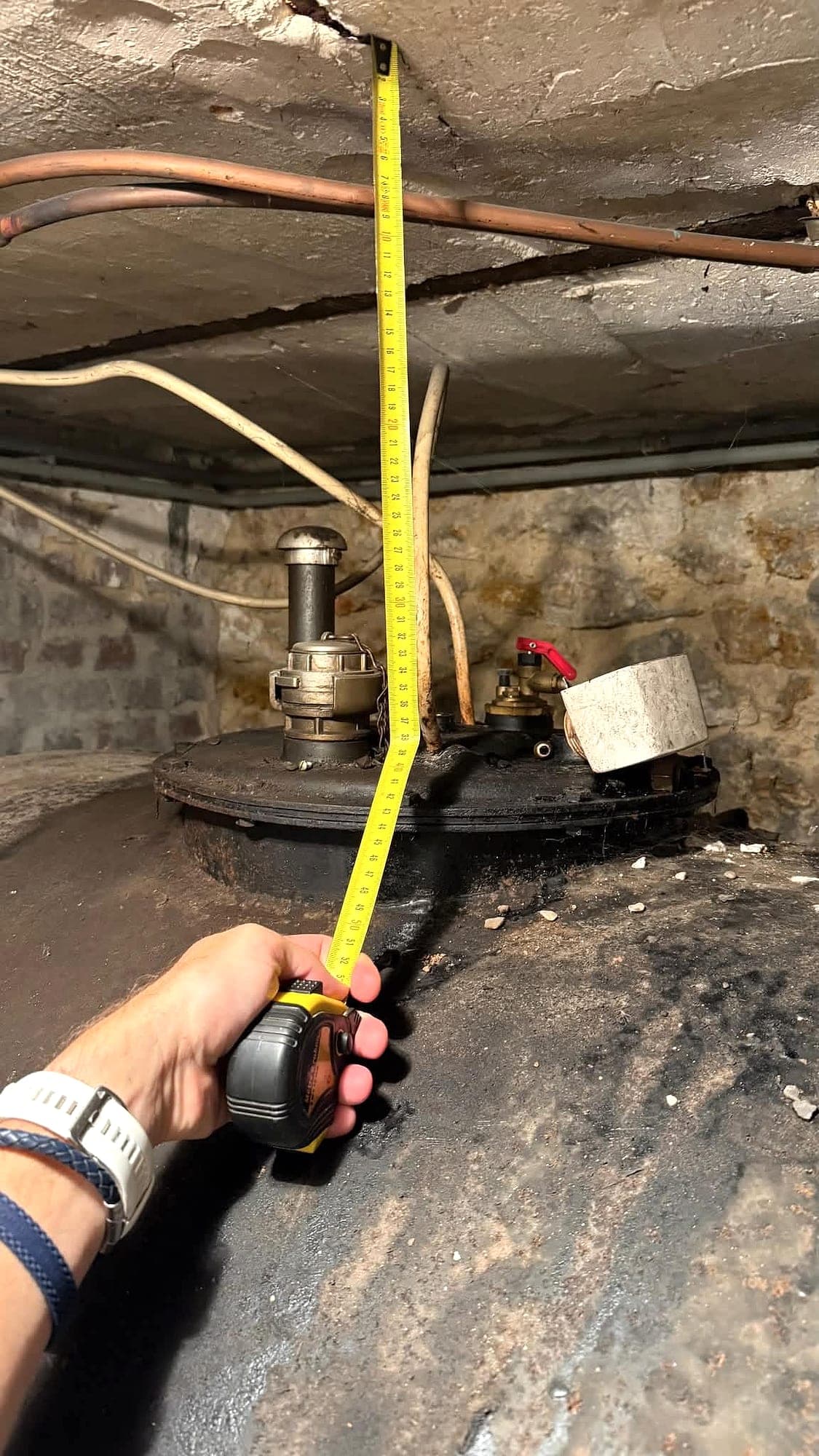 Technicien mesurant au mètre ruban la hauteur libre entre le dessus d'une cuve à fioul et le plafond d'une cave